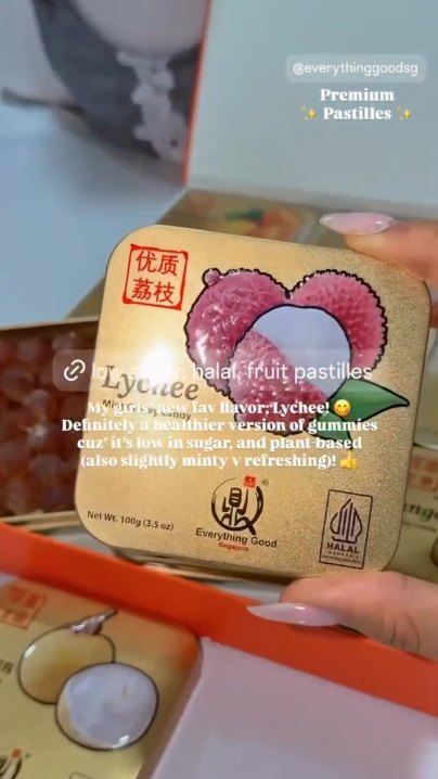 Hand holding an Everything Good Lychee Mint Chewy Candy tin above an open box of assorted flavour tins