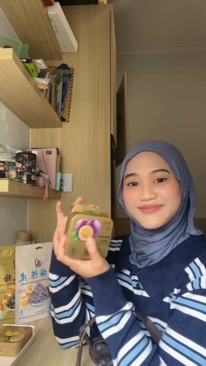 Creator holding an Everything Good Passion Fruit Mint Chewy Candy tin at her desk, with Sour Plum and Waxberry candy pouches beside her