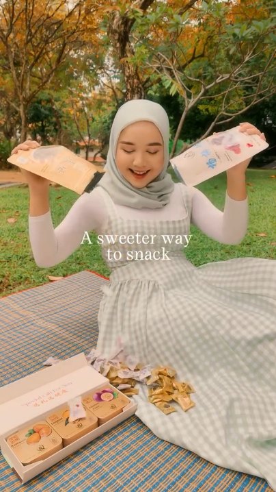 Creator at a picnic holding up Everything Good candy pouches, with an open gift box of Mint Chewy Candy tins on the mat